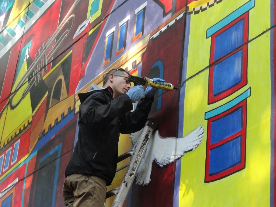 Emmett Lodge on ladder repairing mural COMMUNITY by Anne Marchand
